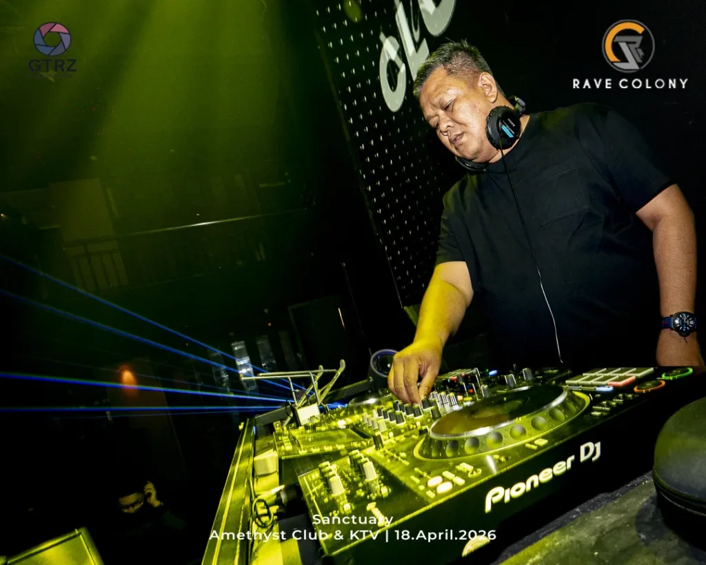 DJ in a black shirt mixes on a glowing Pioneer DJ console at Amethyst Club & KTV, April 18, 2026, with club logos visible in the background.