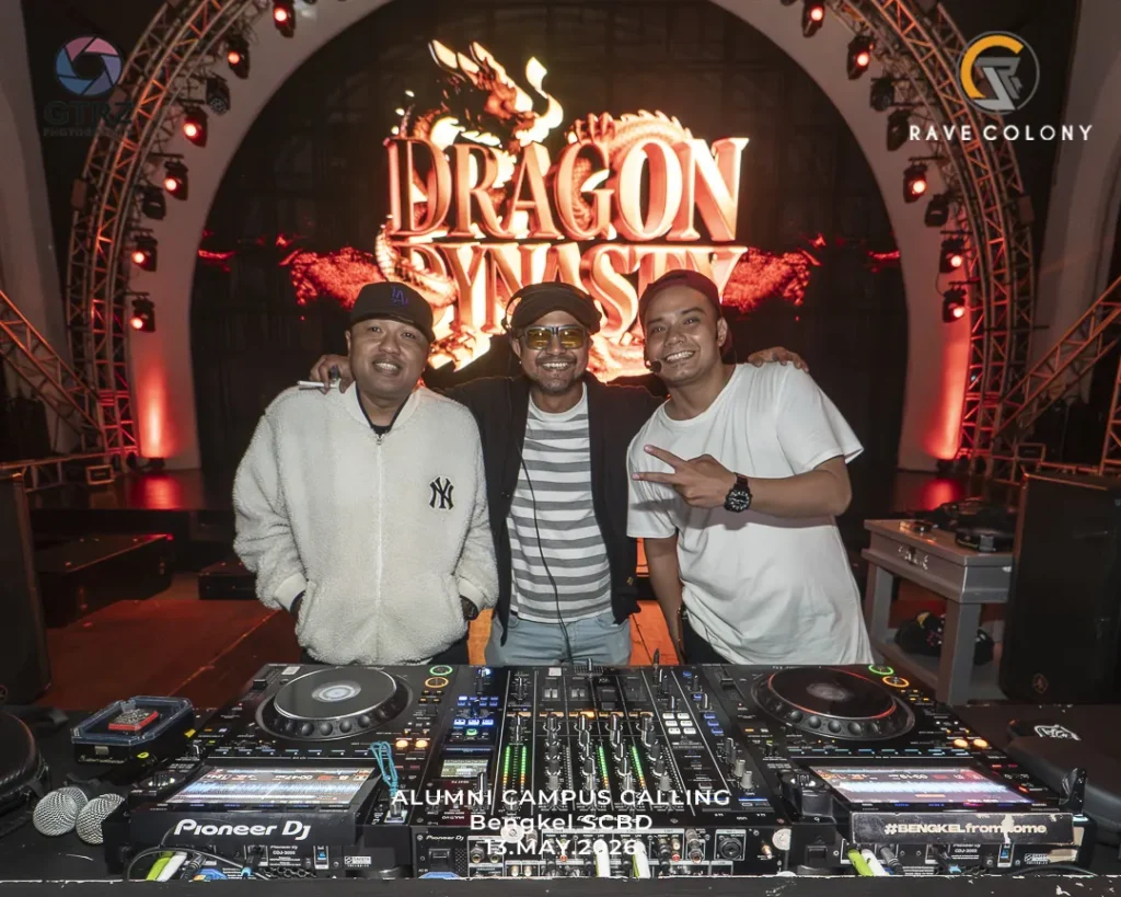 Three men pose behind a Pioneer DJ setup on a stage with a bold Dragon Dynasty backdrop and lighting.