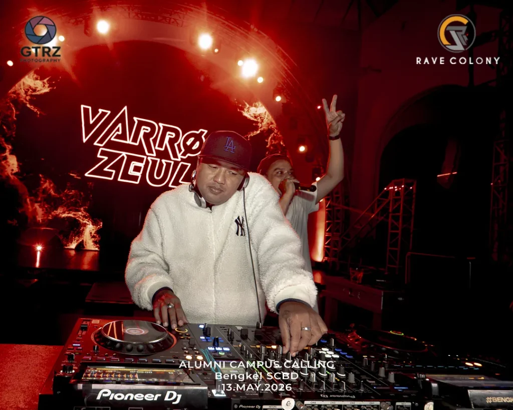 DJ in a white fleece jacket and LA cap mixes on a Pioneer DJ setup on a red-lit stage, with neon 'VARRO ZEUS' graphics in the background and event text at the bottom.