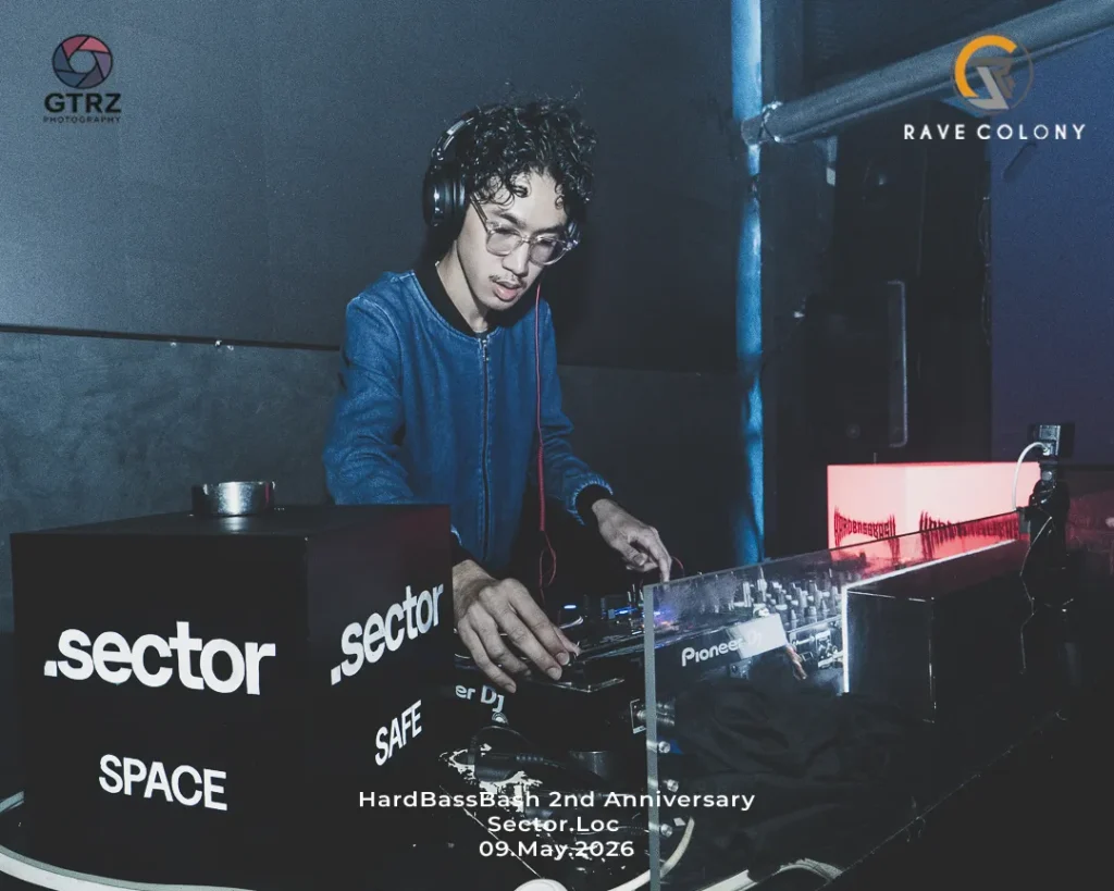 DJ wearing headphones and glasses, mixing at the Sector Space booth with logoed panels in a club setting (HardBass Bash 2nd Anniversary).