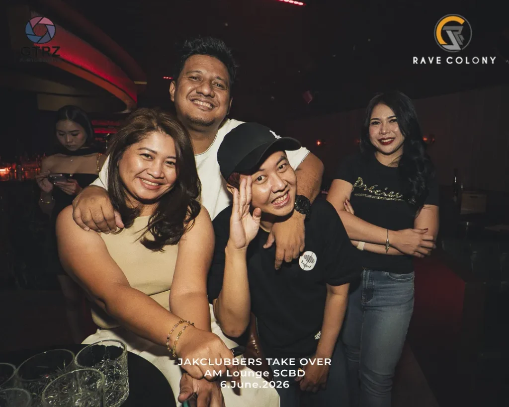 Group of four friends posing together in a dim nightclub, smiling at the camera, with logos visible in the corners and a bottom caption.
