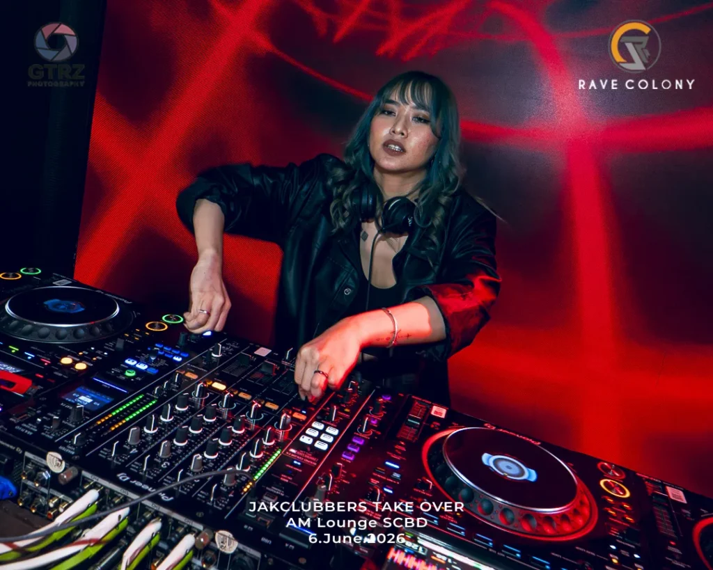DJ in a black jacket mixes on a professional mixer at a club with red stage lighting and event text overlay.