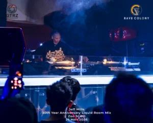 DJ Jeff Mills performing a club set behind a glass booth crowd in foreground with event text and logos on screen