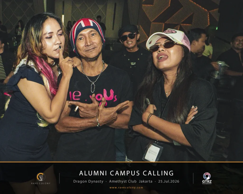 Group of three adults posing and smiling at a party, with a black banner reading 'Alumni Campus Calling' in the foreground.