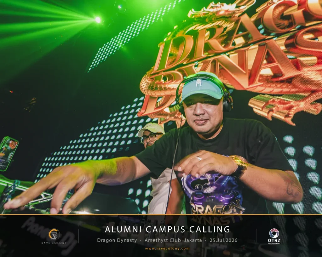DJ wearing a light blue cap and headphones spins records on a crowded green-lit stage, with an event banner reading 'Alumni Campus Calling' in the background.