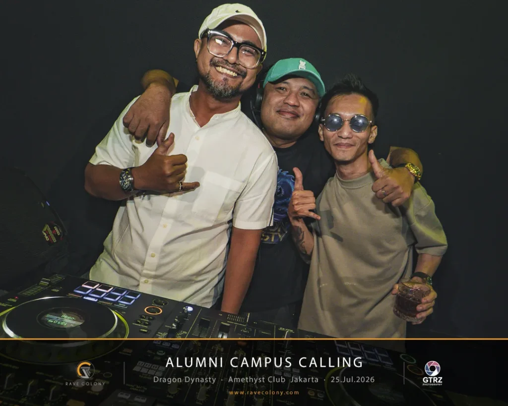 Three men posing together behind a DJ deck at a nightlife event, smiling and giving thumbs up.
