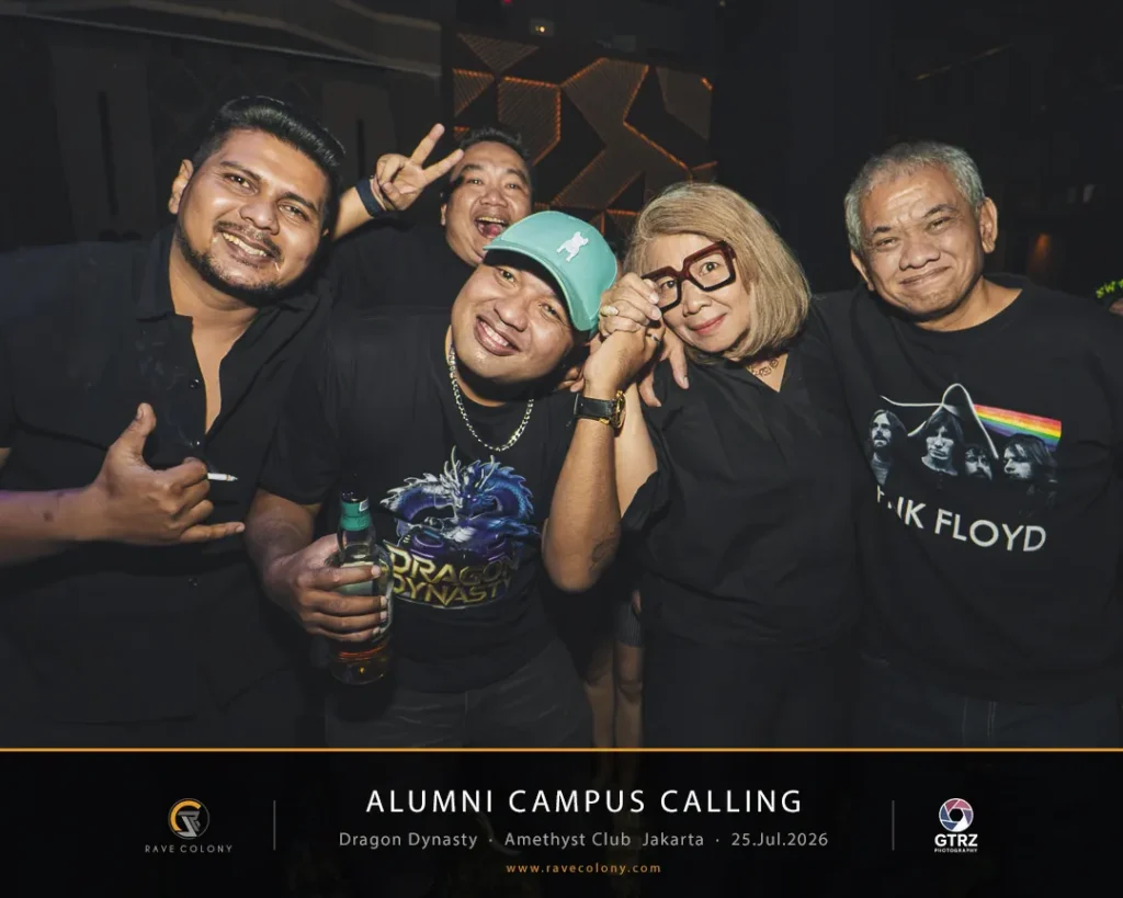 Group of five smiling people posing for a photo at an alumni campus calling event, wearing black shirts; one person holds a bottle and wears a teal cap.
