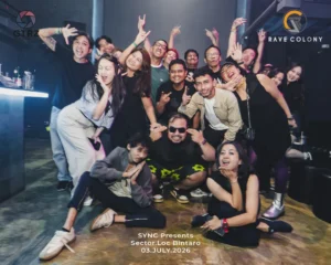 Large group of friends posing and smiling in a nightclub with club logos visible Rave Colony in the background