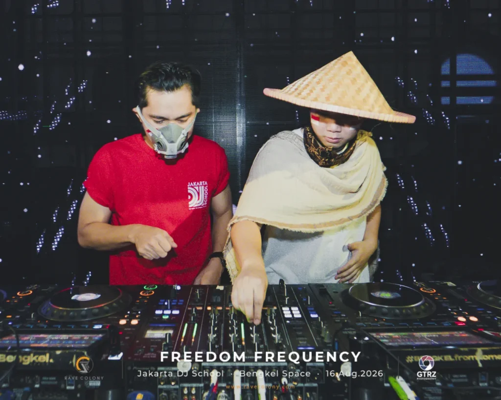 Two DJs perform behind a large mixer, one wearing a red shirt and a mask, the other in a conical hat; event banner reads 'Freedom Frequency' in Jakarta.
