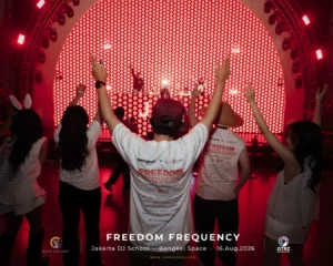 Audience with raised hands in a red-lit venue, watching a DJ on a circular LED stage at the Freedom Frequency event.