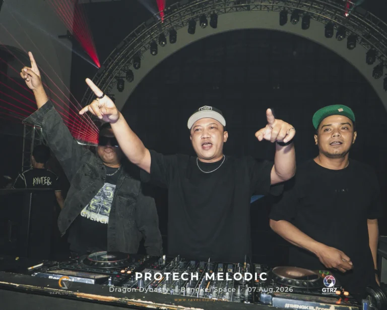 Three male DJs perform at a club, standing behind a mixer with red laser lights overhead.