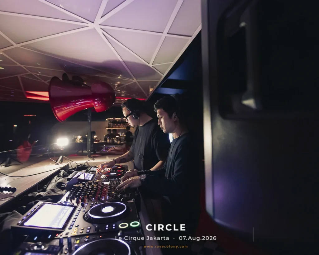 Two DJs mix on a large club DJ setup, with colorful lighting and a red speaker overhead, performing at Circle in Jakarta.