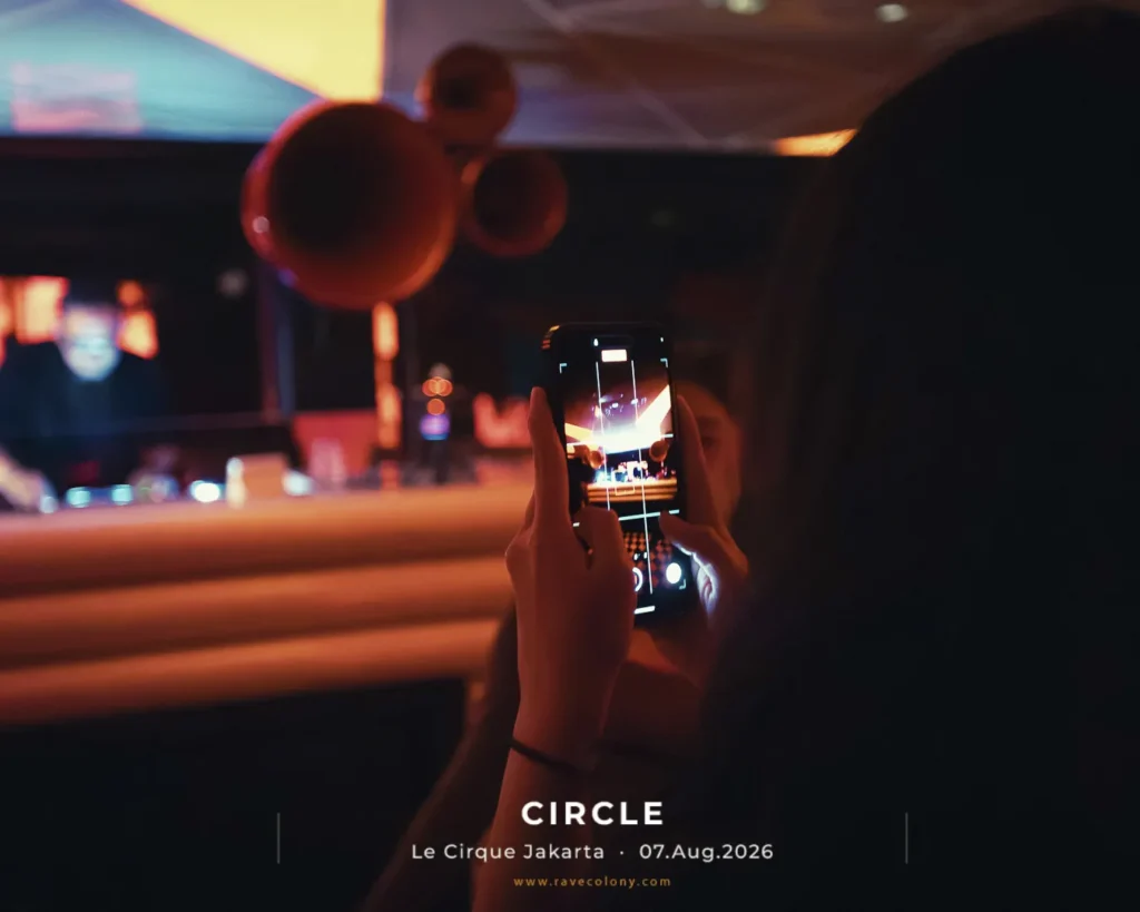 Person filming a live show with a smartphone at Circle Le Cirque Jakarta on 07 Aug 2026, dim stage lighting in the background.